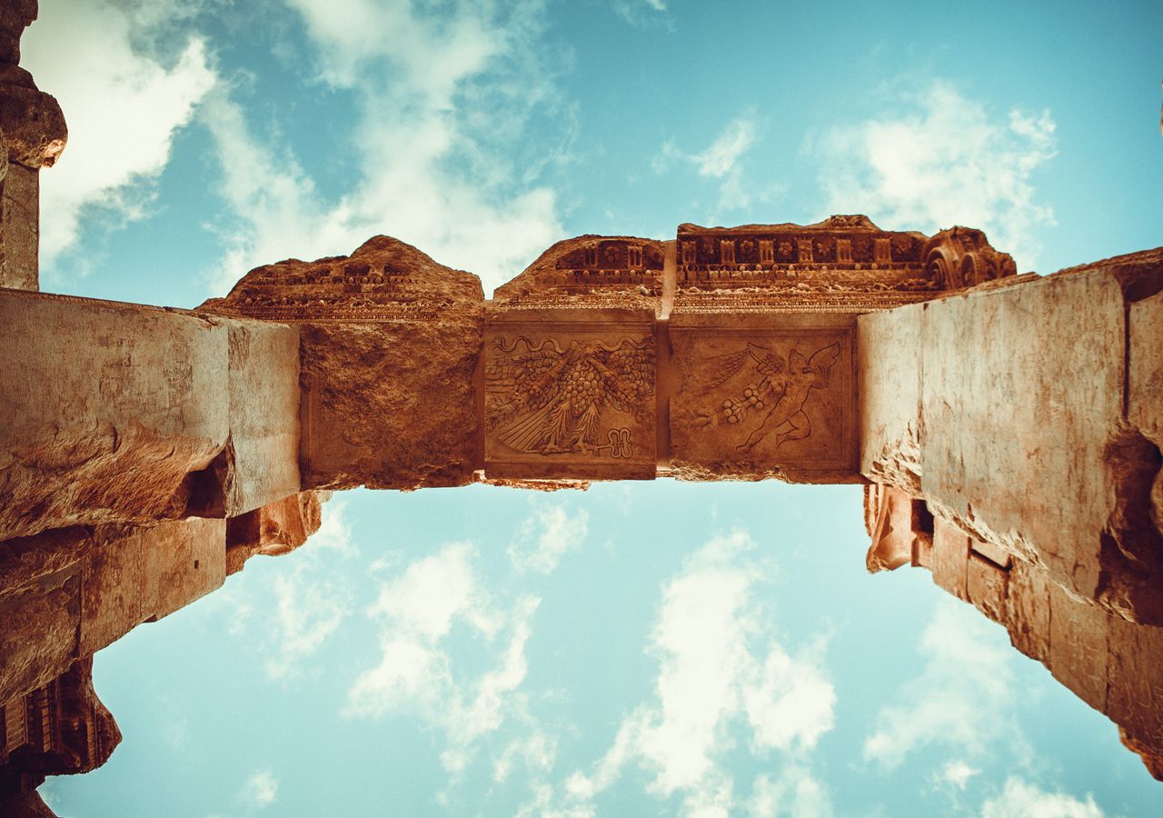 Low angle view of ancient Roman ruins against a blue sky with clouds.